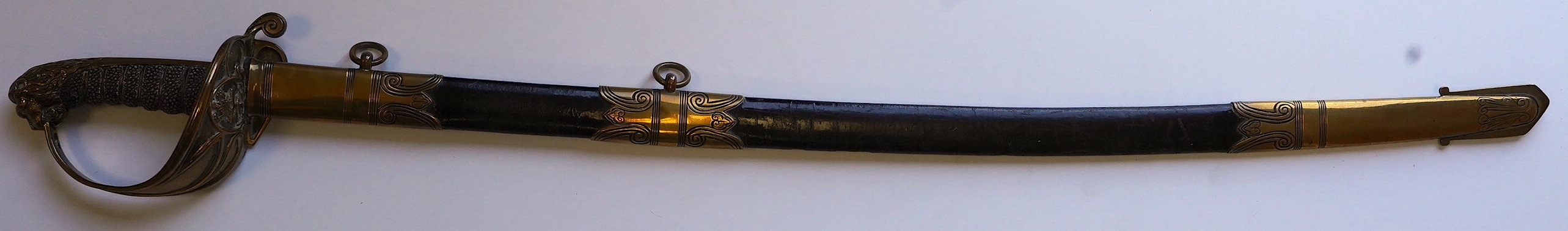 An early 19th century Royal Navy officer's sword with engraved blade, folding knuckle guard, lion’s head pommel and shagreen grip, leather scabbard with brass fittings, blade 73.5cm. Condition - fair, some wear overall.